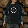 Hombre con camiseta negra personalizable 'Tu Logo Aquí' en diseño circular blanco, sobre fondo de troncos de leña apilados. Ideal para marcas, empresas y uniformes corporativos y profesional.